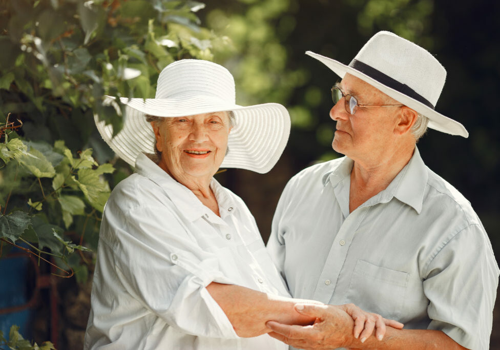 Adult couple in a summer garden. Handsome senior in a white shirt. Woman in a hat.