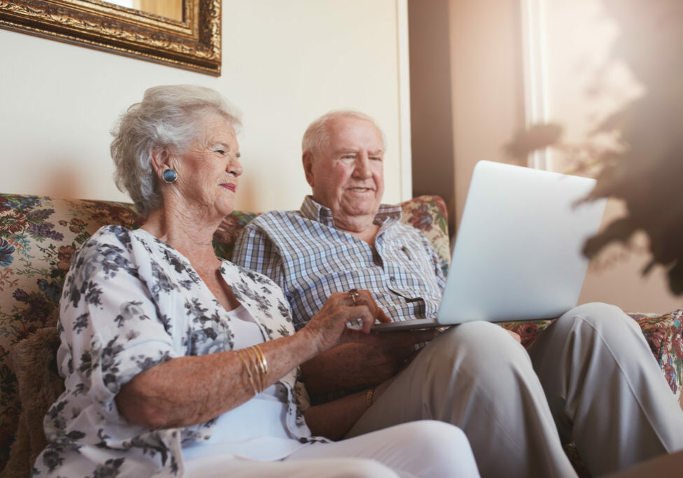 Elderly couple using laptop computer at home. Senior man and woman sitting on sofa working on laptop.