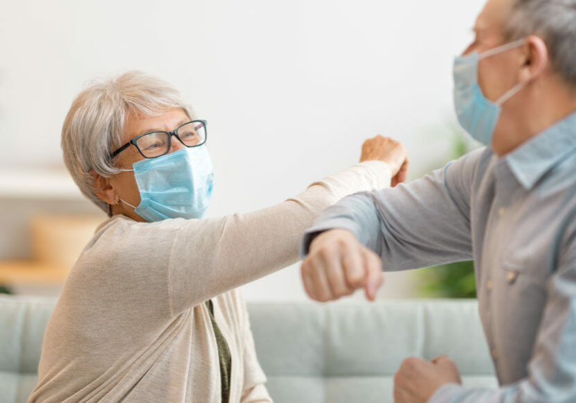 Senior couple wearing face masks and greeting bumping elbows during coronavirus and flu outbreak. Virus and illness protection, home quarantine. COVID-2019.